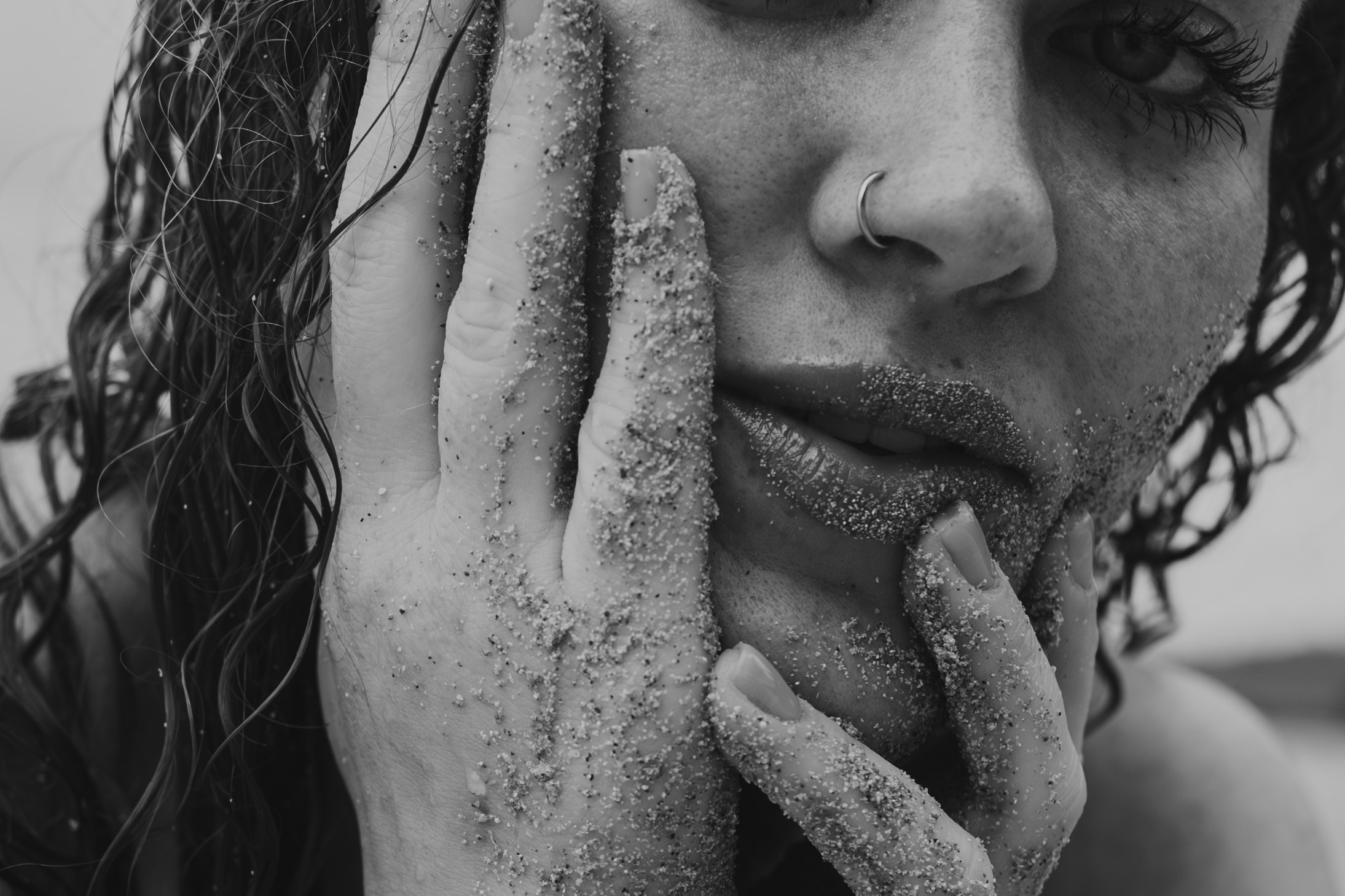 a closeup, black and white photo of a woman's lips and fingers covered in sand. boudoir photos rule.
